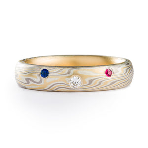 Mokume Gane ring made by arn krebs, twist pattern, made of layers of yellow gold palladium and non oxidized silver, has 3 flush set stones set into the band, all round, white in the center and red and blue on either side