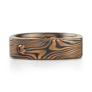 mokume gane flat profile band for a modern combination with the natural style of mokume gane pattern, shown here in twist pattern and with a small cognac diamond flush set towards the left edge of the ring