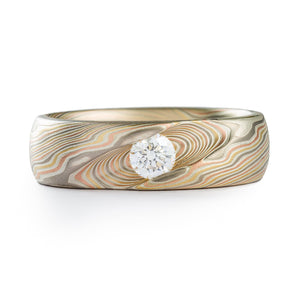 Custom designed ring, a round diamond is nested in a diagonal cut channel, that echoes the direction of the twisting pattern that runs around the ring. Metals in the ring are layers of silver alternated with palladium, red gold, and yellow gold