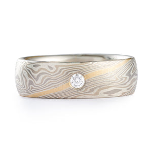 This Mokume Gane ring is shown in the Twist pattern and the Smoke metal combination. It also features a flush set diamond, a low-dome profile, and an etched finish. The Smoke palette features 14k White Gold, Palladium and Sterling Silver. This ring also has a beautiful added 14k yellow gold stratum.