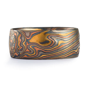 This rustic feeling Mokume Gane band is shown in the Twist pattern and the Firestorm metal combination, with a low dome profile and an etched and oxidized finish. Our Firestorm palette features 14k red gold, 14k yellow gold, palladium, and sterling silver. The twist pattern and multicolor of the Firestorm palette bring to mind the rough and diverse terrain of the earth ,and this extra wide band offers lots of real estate to show off the patterning!