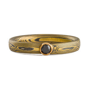 mokume gane ring by arn krebs in spark metal palette and woodgrain pattern with bezel set black diamond