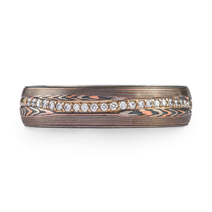 mokume gane patterned ring, red gold palladium and oxidized silver, with a line of diamonds set in the center of the band. The line gently curves around the patterning.