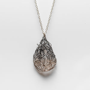 Teardrop shaped spun wire pendant hanging on a chain. Both chain and pendant are silver, with gradual oxidation towards the top of the teardrop.