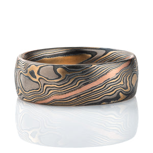 Wide men's style mokume gane band, patterned in twisting style, made with mainly yellow gold, palladium and oxidized silver, with one stripe of red gold.