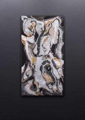 Vertically oriented rectangular wall art, hanging on a gray wall, made of swirling colors of black, silver, gray and gold, with textured details.
