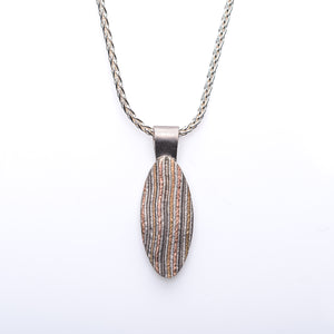 Long eye shaped pendant hanging vertically on a chain, patterned in mokume gane in a striped style.