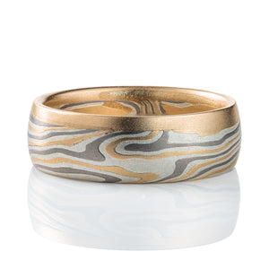 Mokume gane ring made of twisting layers of oxidized silver, palladium and yellow gold, with a solid strip of yellow gold running around one edge.