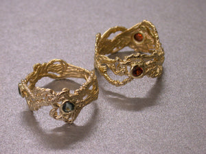 two solid gold rings cast to look like interwoven strands and threads, with small round stones set into bezels in the rings.