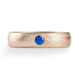 simple and lovely mokume gane wedding ring in fire palette with red and yellow golds and blue sapphire flush set in
