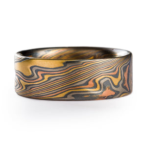 Flat profile 8mm wide Mokume Gane ring made by arn krebs, twisting pattern running diagonally across the band, the ring is made up of alternating layers of yellow gold red gold and palladium with layers of oxidized silver in between each 