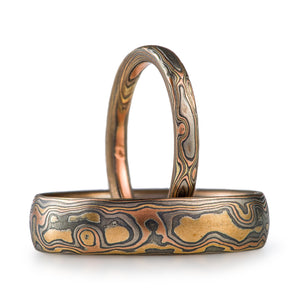 set of matching mokume gane rings in 4 metal combination of red gold yellow gold palladium and oxidized silver with a woodgrain pattern