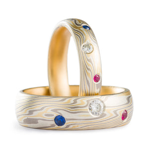 Matched set of mokume gane rings, made of yellow gold palladium non oxidized silver, both rings have 3 flush set stones each, a moissanite ruby and sapphire