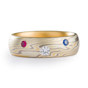 Mokume Gane ring made by arn krebs, twist pattern and made of yellow gold and palladium alternating with layers of non oxidized silver, three stones flush set, larger white one in the center and red and blue on either side