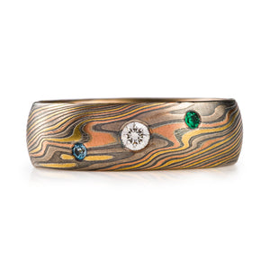 Mokume gane wedding band with added flush set gemstones, center stone is a diamond and sides are blue and green stones, arn krebs firestorm palette