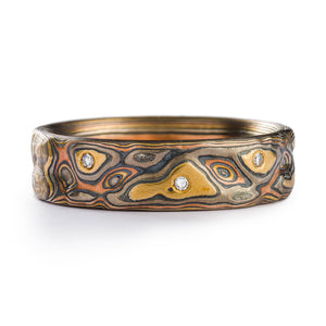 Mokume Gane ring made by Arn Krebs, layers of gold red gold and palladium alternated with oxidized silver. The surface of the ring has been carved into to resemble topography and there are small diamonds flush set in and placed organically across the ring