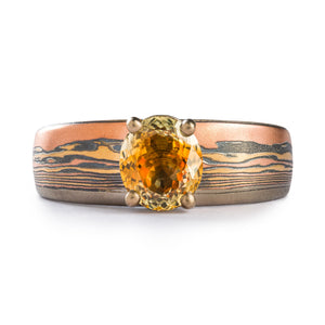 This gorgeous, unique, Mokume Gane engagement ring is shown in the Fire metal combination and a custom pattern made to resemble a landscape and create a sunset scene effect with the beautiful sapphire.