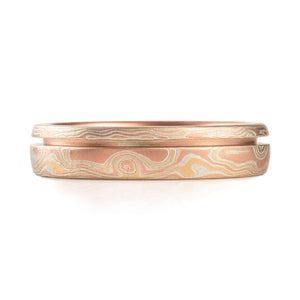 mokume gane patterned ring, with an inset line of red gold, creating an indent running horizontal around the ring, cutting through the pattern, ring is predominantly red gold, with yellow gold and silver.