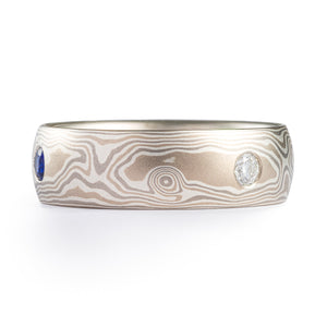 This classic feeling Mokume Gane ring is shown in the Woodgrain pattern and the Smoke metal combination, with a low dome profile, satin finish, and flush set diamonds and sapphire.