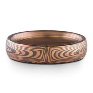 mokume gane band in vortex pattern oxidized fire palette, red gold yellow gold and oxidized silver layers form an asymmetrical pattern meeting at the center of the ring, on a white background