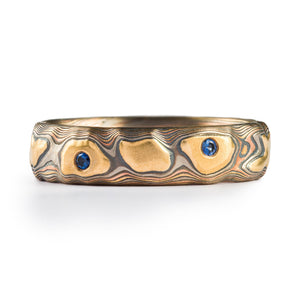 guri bori style mokume gane ring, carved patterning that resembles a topographic map and landforms, small blue gems flush set into the ring