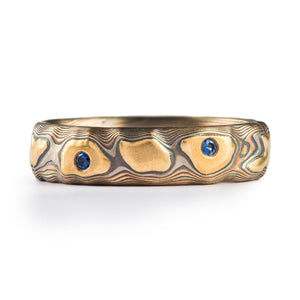 guri bori style mokume gane ring, carved patterning that resembles a topographic map and landforms, small blue gems flush set into the ring
