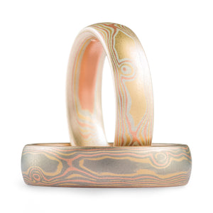 Two mokume gane woodgrain patterned rings, one is lighter looking with a more yellow gold palette, the other is darker with a white gold dominated palette