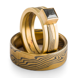 three piece wedding set of mokume gane rings, one has yellow gold ring guard with a salt and pepper diamond
