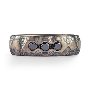 black diamonds flush set or bead set into a Mokume Gane ring with layers of grey and black metal 