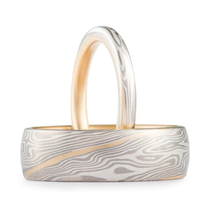 Two matching mokume gane rings, twist patterning with palladium and silver, one thin ring, one wide ring, both have a yellow gold layer and a yellow gold lining.
