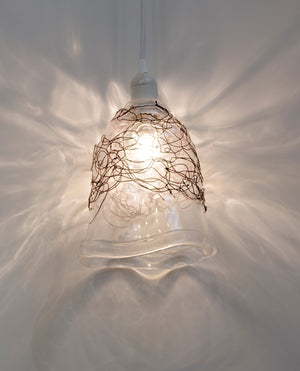 Clear blown glass pendant light bell shape accented by woven blackened copper wire scribble lines on the top half of the bell shape. Hangs from a white cord. Lighting, home decor, interior design